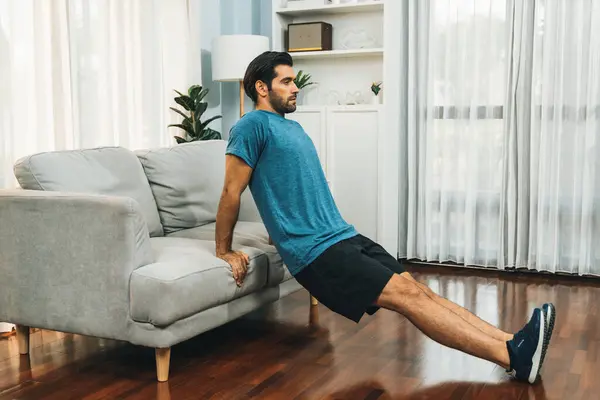 健康的なフィットボディホームワークアウトのライフスタイルのコンセプトとして 効果的なターゲティング筋肉の運動のための家具を使用して運動体とアクティブスポーティーな男性 — ストック写真