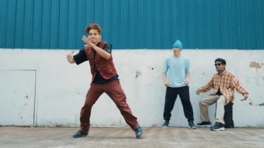 Genç Asyalı dansçı hip hop tarzında dans ediyor ve çok kültürlü arkadaşları duvarın arkasında tezahürat yapıyor. Çekici yakışıklı adam mavi arka planda kollarını uzatıyor. Açık hava sporu 2024 hiphop..