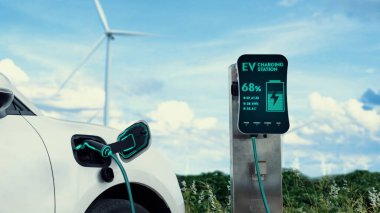 Elektrikli araba, rüzgar türbini çiftliğinde çalışan akıllı EV şarj cihazıyla şarj edilen enerjiyi şarj ediyor. Alternatif temiz sürdürülebilir enerjinin teknolojik ilerlemesi. İnceleyin