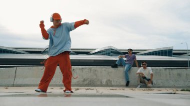 Briçte kendine güvenen bir şekilde kameraya poz verirken, hip hop 'çı adam kulaklık takıyor. Aktif enerjik yenilikçi arkadaş arkada tezahürat yaparken serbest dans ya da ayak sesi yapar. Açık hava müziği 2024. Yumuşak bir şekilde..