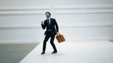 Profesyonel proje yöneticisi, beyaz arkaplanlı canlı müziğe geçerken başarı projesini kutlamak için dans ediyor. Dans ederken çantasını tutan yetenekli bir iş adamı. Hareket atışı. Uzayı kopyala Sevinçli..