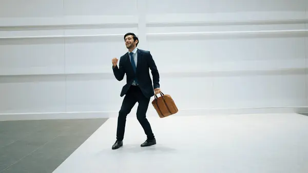 Professional project manager dancing to celebrate success project while moving to lively music with white background. Skilled business man holding bag while dancing. Motion shot. Copy space. Exultant.