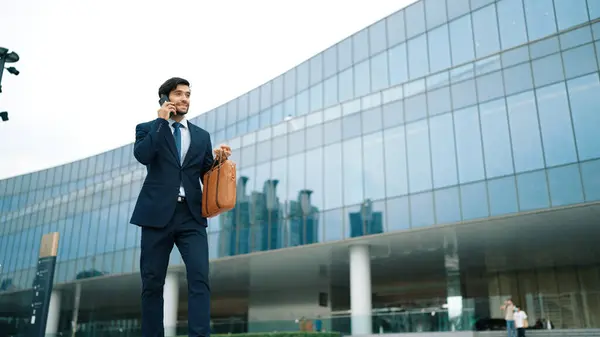 Smart business man using phone to talking while walking at building. Happy manager walking at street while talking on smart phone to discuss business plan or marketing strategy or working. Exultant.