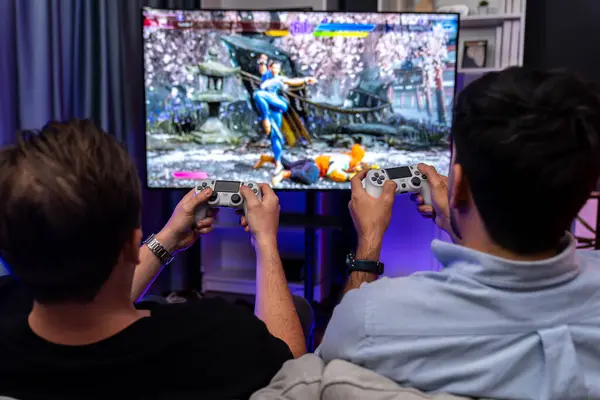 Friend gamers playing video game of battle martial arts fighter on TV using joysticks position of backside background. Comfy living neon light at home place with cheerful fighting winner. Sellable.