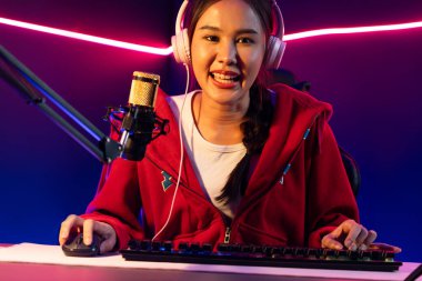 İnternet üzerinden kulaklık takıp gülümseyen Asyalı güzel kız flamasının sunucu kanalı izleyicilerle internet üzerinden konuşma yapıyor. Esport yetenekli takım oyuncuları neon mavi odada. Taktik.