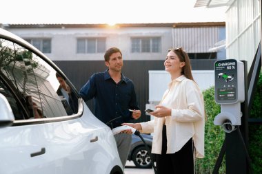 Çevre dostu aile çifti EV 'yi şarj istasyonundan şarj ediyor. EV elektrikli araba teknolojisi gelecekteki sürdürülebilirlik için alternatif ulaşım olarak kullanılıyor. Yararlı