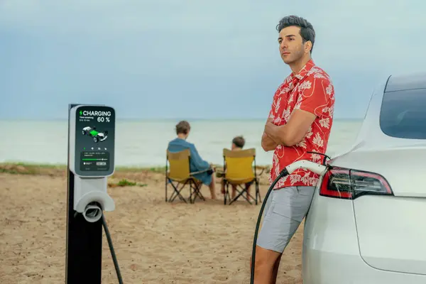 乘坐电动车在海滩上旅行的家庭度假旅行 父亲或父亲给电动车充电 而他的家人则享受海景海滩 采用替代能源和环保汽车的家庭旅行 永远不变 — 图库照片