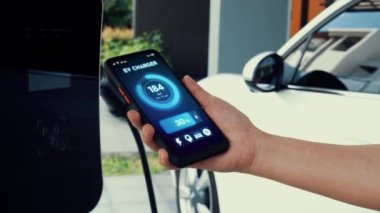 Akıllı telefon ekranı akıllı EV mobil uygulama üzerinde pil durumu EV araba garajdaki ev şarj istasyonu ile elektrik şarj ederken. Geleceğin yenilikçi EV arabası ve enerji sürdürülebilirliği. İnceleyin