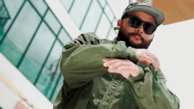 Asyalı hippi gökyüzü dövüşçüsüne dans ederken kameraya bakıyor. Modern AVM 'de düşük açılı kamerayla hip hop müziğine ayak basan çekici yakışıklı hippi. Dans edelim. Açık hava sporu 2024 hiphop..
