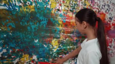 Genç mutlu kız renk tepsisini tutuyor ve fikri ifade etmek ve el iziyle hayal gücünü geliştirmek için renkli duvarları boyuyor. Resim dersinde odayı dekore etmek için beyaz kız pulu. Öğretim