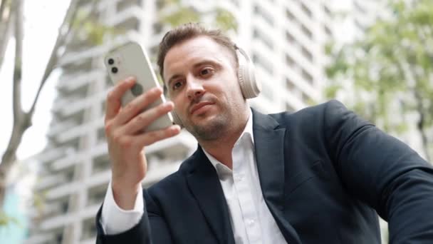 Smart Kaukasisk Affärsman Bära Hörlurar Samtidigt Kontrollera Mobiltelefon Och Ser — Stockvideo