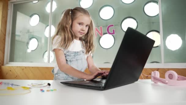 ラップトップを使用して働いたり ゲームをしたりする小さなかわいい少女 カメラを見ながら笑顔でコンピューターで作業する学生 子供はヘッドフォンを使用してオンラインクラスに参加します エラー — ストック動画
