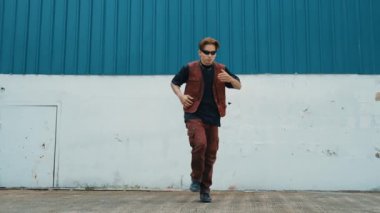 Beyaz arka planda break dans pratiği yapan yakışıklı bir sokak dansçısı. Hip hop tarzı giyinen sporcu, mavi arka planlı bir sokakta müzik eşliğinde ayak sesleri çıkarıyor. Açık hava sporu 2024 hiphop..