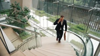 Akıllı iş adamı spiral merdivenlerden yukarı çıkıyor ve akıllı telefon kullanarak müdürü arıyor. Modern binada merdivenleri çıkarken telefonla pazarlama ekibinin üst düzey görüşü. Urbane.