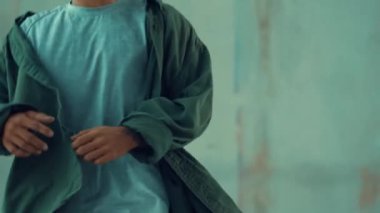 Hippi, şehir caddesinde hip-hop dinlerken kulaklık takıyor. Sokak dansçısı ayak seslerini kulaklıktan müziğe taşıyor. Açık hava sporu 2024. Çimento arka planı. Moda. Aktif stil. hiphop.