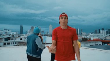 Çok kültürlü veya çok kültürlü hipster grupları şık ve renkli giysiler giyerek çatıda şehir manzaralı ve gökyüzü kazıyıcılarıyla dans ederler. Canlı sokak dansı konsepti. Açık hava sporu 2024 hiphop..