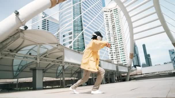 时髦的亚裔男子用低角度相机表演嘻哈舞曲 在城市里一边听耳机里的音乐一边跳起舞 一边跳起舞来跳起舞来 2024年户外运动 神气活现 — 图库视频影像