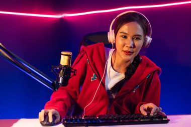 İnternet üzerinden kulaklık takıp gülümseyen Asyalı güzel kız flamasının sunucu kanalı izleyicilerle internet üzerinden konuşma yapıyor. Esport yetenekli takım oyuncuları neon mavi odada. Taktik.