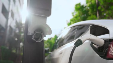 Yazın yeşil sürdürülebilir şehir bahçesinde elektrikli araba şarj oluyor. Kentsel sürdürülebilirlik yaşam tarzı yeşil temiz yeniden şarj edilebilir enerji elektrikli BEV araç iç organları