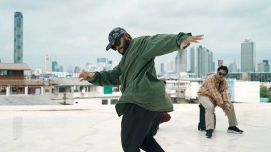 Profesyonel break dans takımı çatıda çok kültürlü arkadaşlar varken break dans alıştırması yapıyor. Genç modern dans grubu hip hop hareketi yapıyor. Tarz, moda, aksiyon. Açık hava sporu 2024. ÇalışmaComment.
