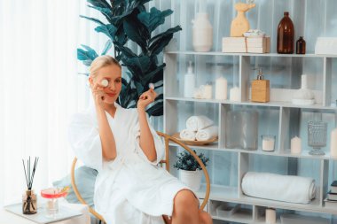 Elinde taze salatalık dilimleri tutan ve bornoz giyen bir kadın tatil köyünde ya da otelde lüks yüz derisi kaplıcalarının tadını çıkarıyor. Yüz ve güzellik tedavisi için cilt bakımı. Sessiz.