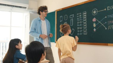 Akıllı çocuk tahtada dururken matematik teorisine cevap yazıyor. Beyaz çocuk sınıfın önünde sınav yaparken çekici erkek öğretmen ilköğretim sınıfına bakıyor. Eğitim. Pedagoji.