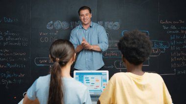 Tahtada çeşitli öğrencilere mühendislik kodları öğreten yakışıklı bir öğretmen. Mutlu çok kültürlü liseli çocuklar dizüstü bilgisayar kullanırken öğreniyor ya da programlama veya kodlama sistemini öğreniyor. Öğretim.