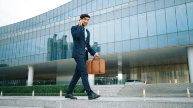Akıllı iş adamı binada yürürken telefonla konuşuyor. İş planı, pazarlama stratejisi ya da çalışma hakkında konuşmak için akıllı telefonla konuşurken sokakta yürüyen mutlu bir yönetici. Sevinçli..