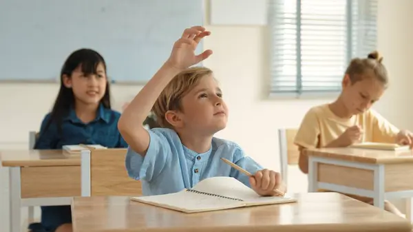 教師が小学校を歩いている間 教室で勉強している多様な子供たちに囲まれた教師を尋ね 答えるために手を挙げる白人の賢い少年 教育コンセプト ペダゴロジー — ストック写真