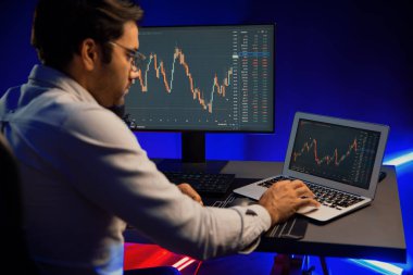 Akıllı tüccar işadamı, karanlık oda gecesinde neon ışıklı ofisteki arama pazarında yüksek kârla ekranda bilgisayar ve bilgisayar üzerinde dinamik borsa yatırımları üzerinde yoğunlaşıyor. Tahmin et..