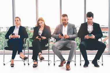 İş kadınları ve işadamları iş görüşmesi için koltuklarda beklerken cep telefonu kullanıyorlar. Şirket işi ve insan kaynakları kavramı. uds