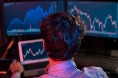 Dizüstü bilgisayara odaklanan genç yatırımcı, güncel pazar grafiğinin dinamik döviz kuru ekranını gerçek zamanlı olarak Neon Light Modern Ofis 'te yatırım yapan iki monitörle karşılaştırıyor. Toplayıcı.