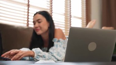 Kanepede yatan genç bir kadın internet bankacılığı için kredi kartıyla dizüstü bilgisayar kullanıyor. Evdeki online ödeme kapısından alışveriş yapıyor. Modern ve uygun online satın alma. Blithe