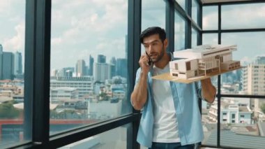 Gülümseyen Kafkasyalı mühendis ev modelini sağa sola çeviriyor ve iş arkadaşına telefon ederken hata noktasını kontrol ediyor. Profesyonel yönetici teftiş, kontrol, mimari modele bakmak. İzleme