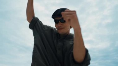 Kameraya alçak açıyla bakarken dans eden Asyalı profesyonel hippi. Şık bir hip-hop dansçısının çatıda müzik dinlemesi. Açık hava sporu 2024. Sokak dansı. Hareket eden kamera. hiphop.