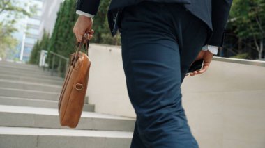 Yeşil şehirde bavulunu tutarken resmi takım elbiseli beyaz bir müdürün merdivenlerden çıkışının arka görüntüsü. Profesyonel bir iş adamı iş yerine giderken aynı zamanda Eko Şehri 'nde merdivenleri çıkıyor. Urbane..