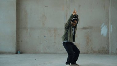 Hippi, şehir caddesinde hip-hop dinlerken kulaklık takıyor. Sokak dansçısı ayak seslerini kulaklıktan müziğe taşıyor. Açık hava sporu 2024. Çimento arka planı. Moda. Aktif stil. ÇalışmaComment.