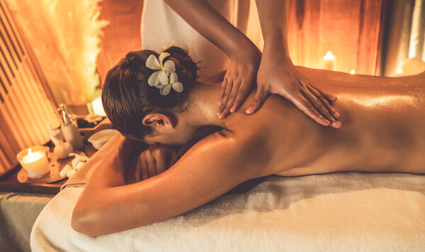 Caucasian woman customer enjoying relaxing anti-stress spa massage and pampering with beauty skin recreation leisure in warm candle lighting ambient salon spa at luxury resort or hotel. Quiescent