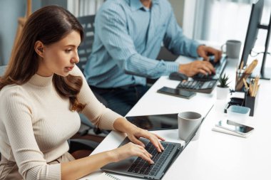 Laptop yazan güzel bir kadının araştırma finansal bilgi raporunu analiz etmek için sabahları modern ofiste masa başında çalışan zeki bir iş arkadaşının yanına odaklanması. Varsayım.