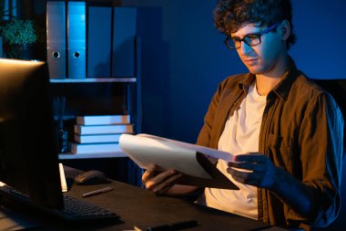 Genç işadamı, Neon Light Modern Ofis 'teki yeni proje surround çalışma masası için kağıt üzerinde tasarım düşünüyor. E-posta ile hediye göndermeden önce not defterine yeni bir iş düşünüyorum. Toplayıcı.