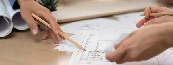 Cropped image of professional architect engineer hand pointing at blueprint by using pencil while colleague measure and analyze house construction. Creative design and teamwork concept. Burgeoning.