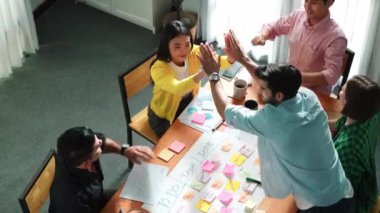 Yaratıcı başlangıç ekibinin takım çalışmalarını veya başarılı projelerini teşvik etmek için beşlik çakarken, aynı zamanda not ve yapışkan notlar kullanarak iş akışını yönetmek için yoğun bir görev tahtası yapmasının en üst görünümü. Cemaat.