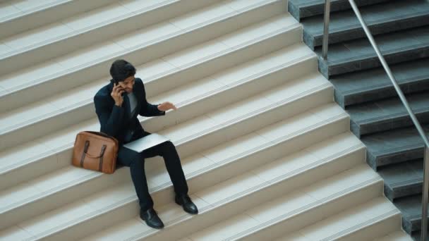 将笔记本电脑放在膝下时 智能商人电话呼叫团队的头像 通过电话与同事交谈或讨论时 专业项目经理坐在楼梯上 工作空间 膨胀剂 — 图库视频影像