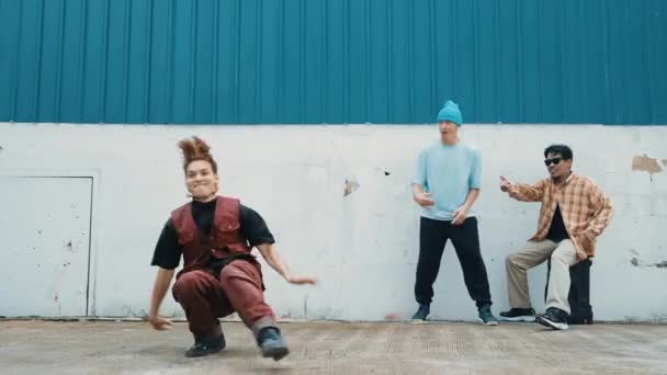 年轻的亚洲舞者跳嘻哈风格的舞 多文化的朋友在墙后欢呼 迷人英俊的男人在蓝色背景的大街上伸出手来 户外运动2024 — 图库视频影像