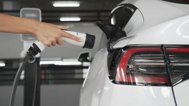 Genç adam EV elektrikli arabasıyla şehir merkezindeki alışveriş merkezinin otoparkına gidiyor şehir merkezindeki sürdürülebilirlik yaşam tarzını yeşil, temiz, yeniden şarj edilebilir elektrikli araç iç organlarıyla şarj ediyor.