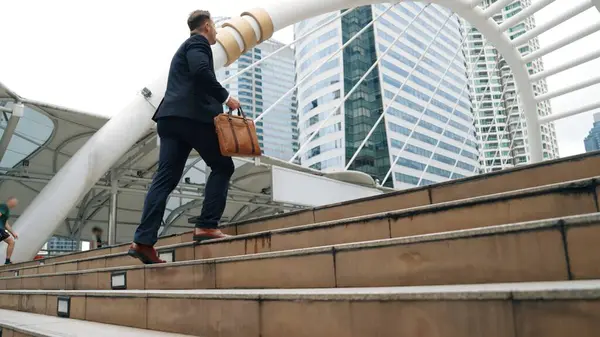 Smart caucasian businessman walking up stairs surrounded by urban view. Side view of ambitious project manager finding challenging job or investment opportunity at city with modern building. Urbane.