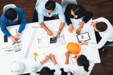 Mimari proje üzerinde birlikte çalışan, inşaat planını gözden geçiren ve toplantı masasında plan oluşturan çeşitli inşaat mühendisi ve müşteri gruplarından oluşan üst düzey bir pankart. Tedbirli