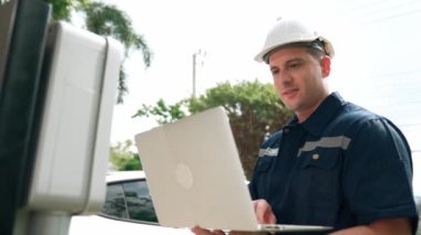 Evde EV şarj istasyonu kurulumu üzerinde çalışan nitelikli teknisyen, EV için dizüstü bilgisayarla şarj sisteminde sorun çıkarma ve yapılandırma ayarları yapıyor. Titiz