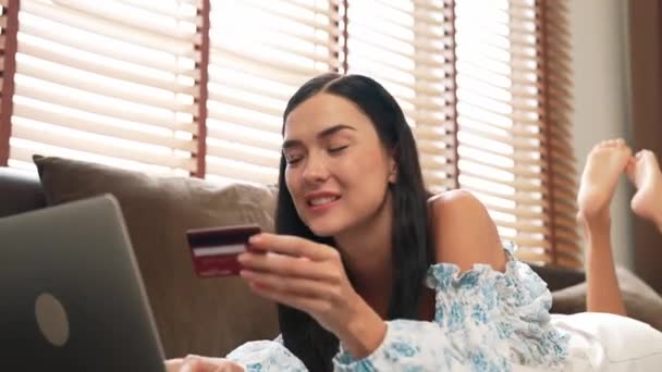 インターネットバンキング用のクレジットカード付きのラップトップを使用してソファに横たわる若い女性 自宅でオンライン決済ゲートウェイでオンラインショッピングEコマース モダンで便利なオンライン購入 ブリテット — ストック動画