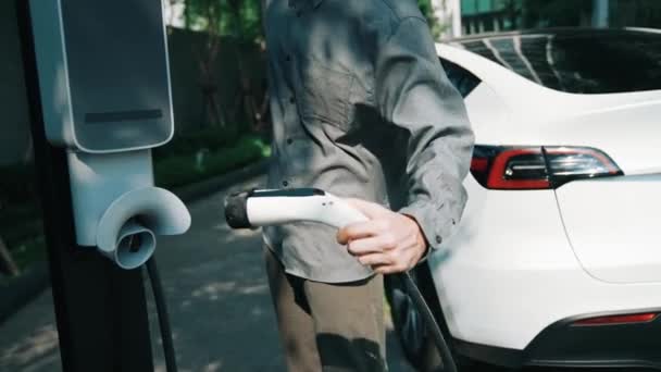 電気自動車都市通勤施設のための持続可能な緑の再生可能なクリーン エネルギーのライフスタイルとスマートな家の住宅Ev充電ステーションで電気自動車の電池を充電する遅い動きの男 — ストック動画